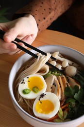 Woman eating delicious ramen with chopsticks at wooden table, closeup. Noodle soup