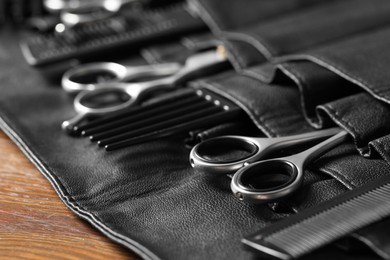 Hairdresser tools. Professional scissors and combs in leather organizer on wooden table, closeup