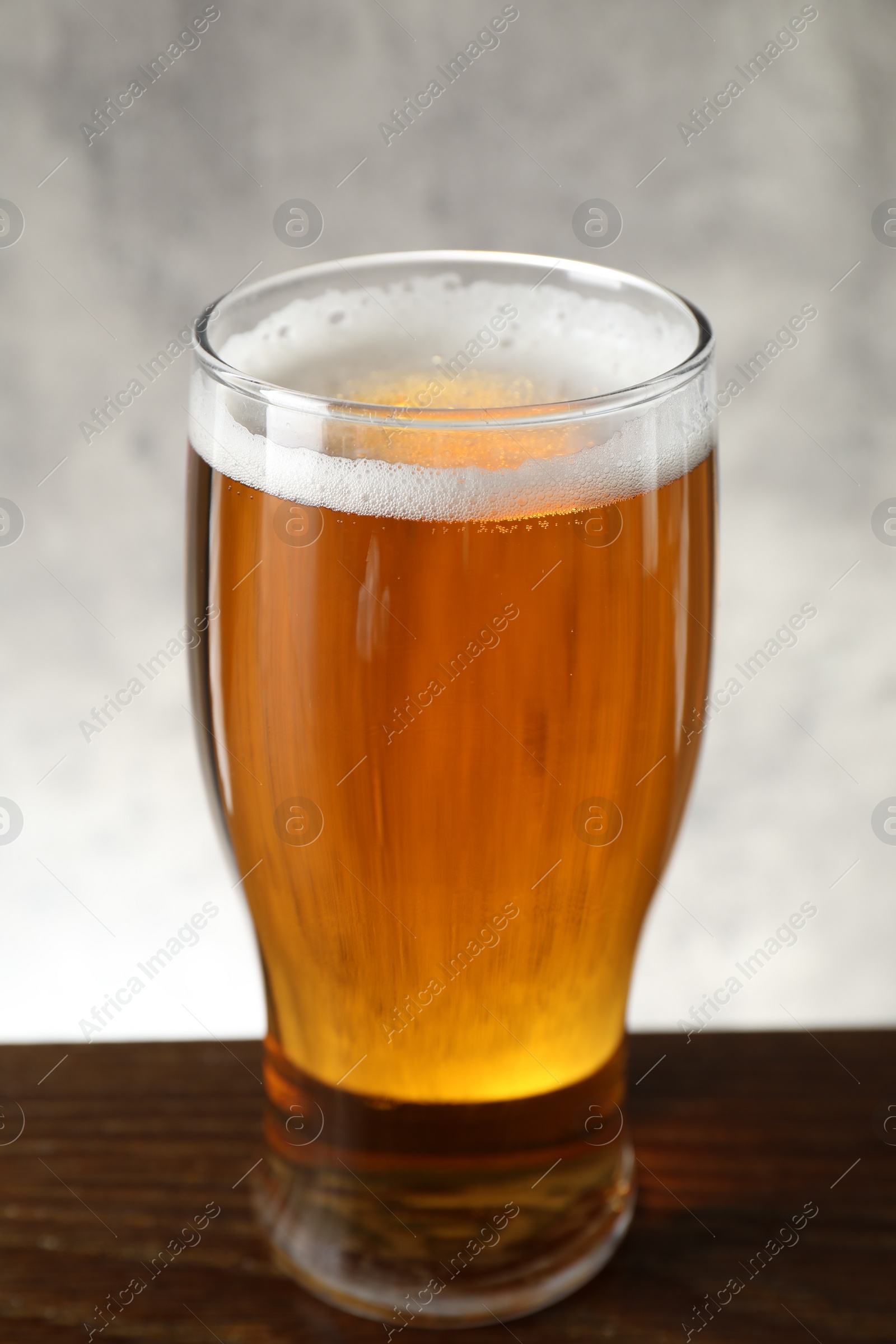 Photo of Glass with fresh beer on wooden table against light background, closeup