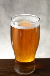 Glass with fresh beer on wooden table against light background, closeup