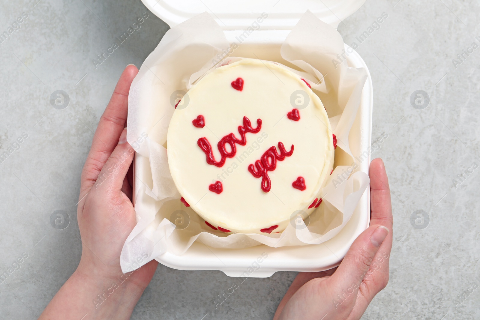 Photo of Woman holding takeaway box with bento cake at light grey table, top view. St. Valentine's day surprise