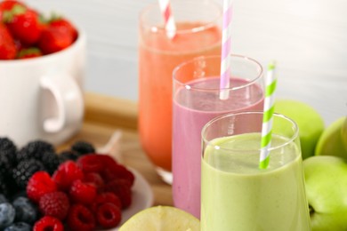 Photo of Glasses of different tasty smoothies and fresh ingredients on wooden tray, closeup