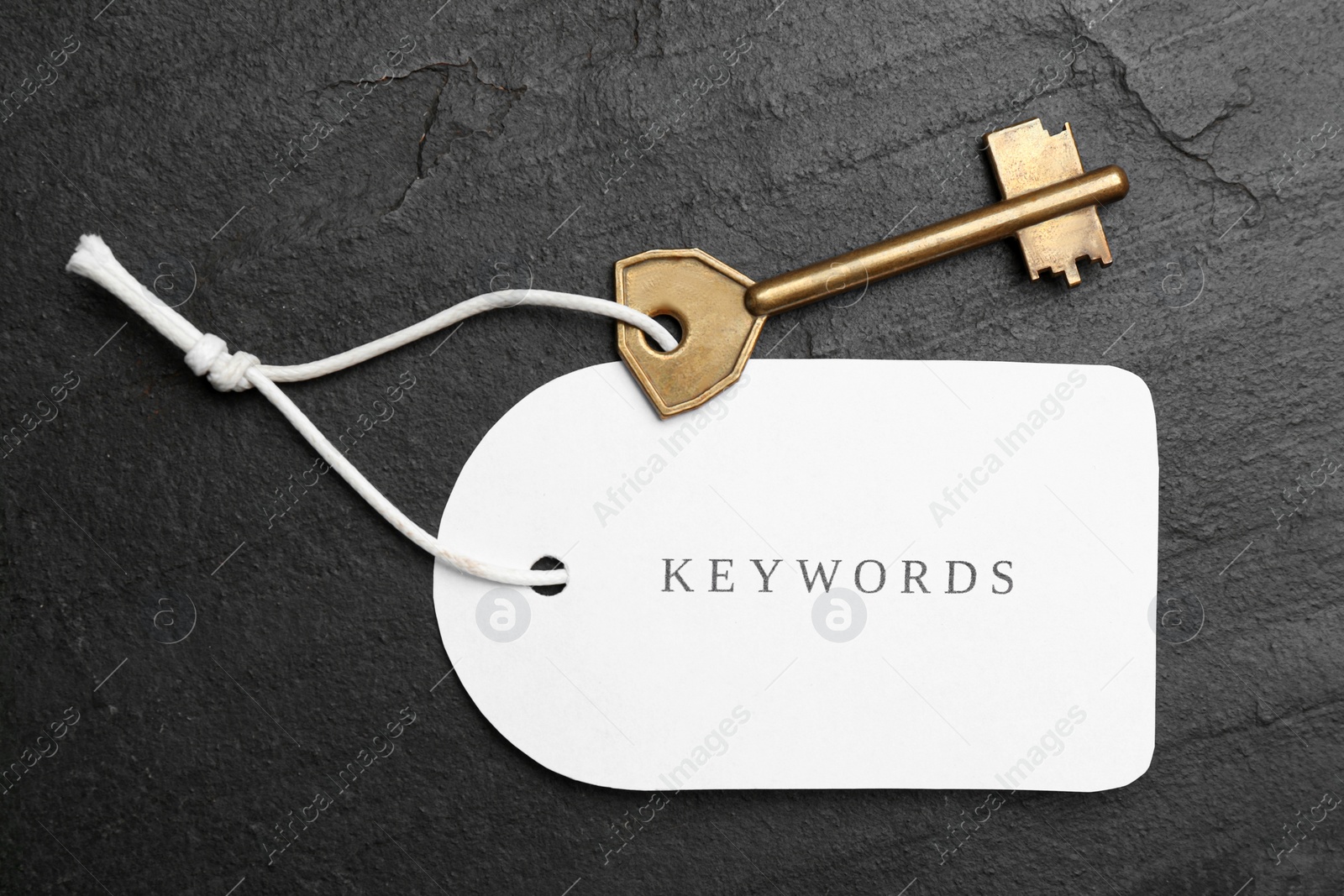 Photo of Metal key and tag wIth word KEYWORDS on black table, top view