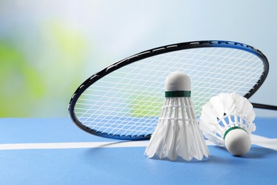 Feather badminton shuttlecocks and racket on blue table against blurred background, closeup