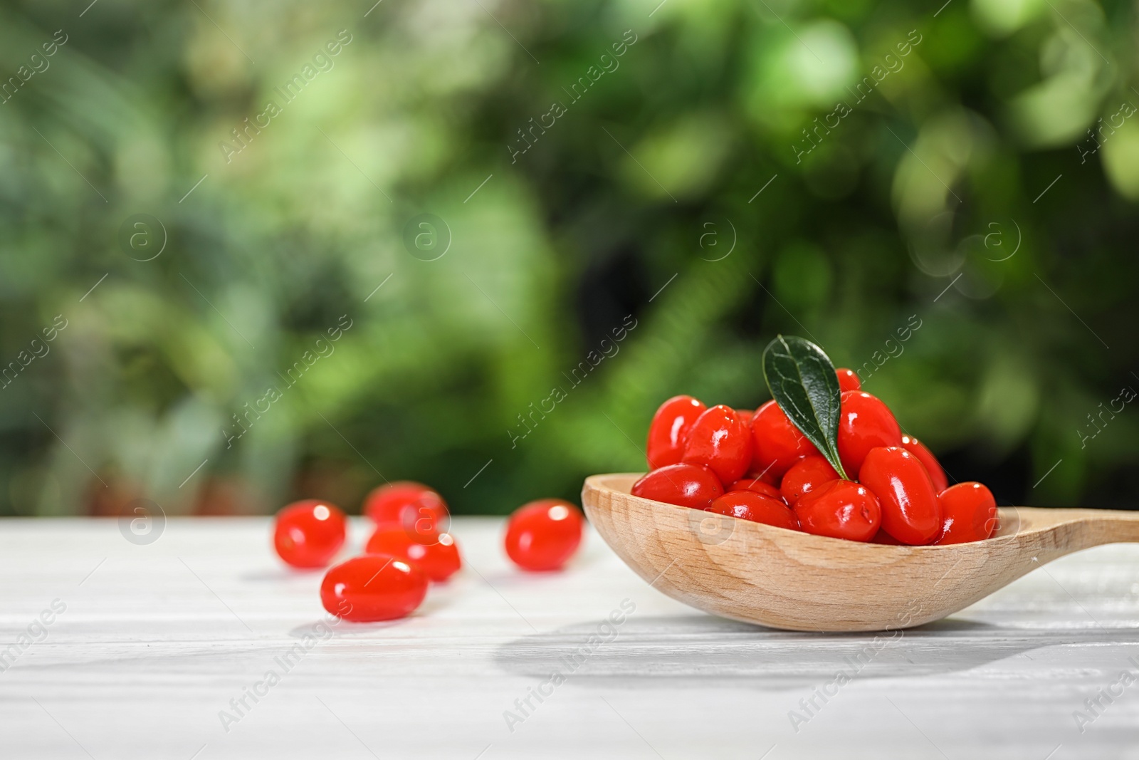 Photo of Spoon with fresh goji berries on white wooden table against blurred background. Space for text