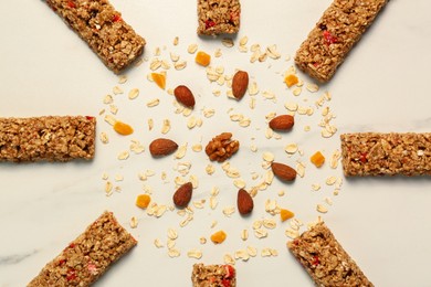 Photo of Sun made with tasty granola bars, nuts and oat flakes on white marble table, flat lay