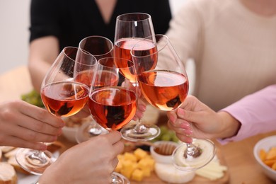 People clinking glasses with rose wine above table indoors, closeup