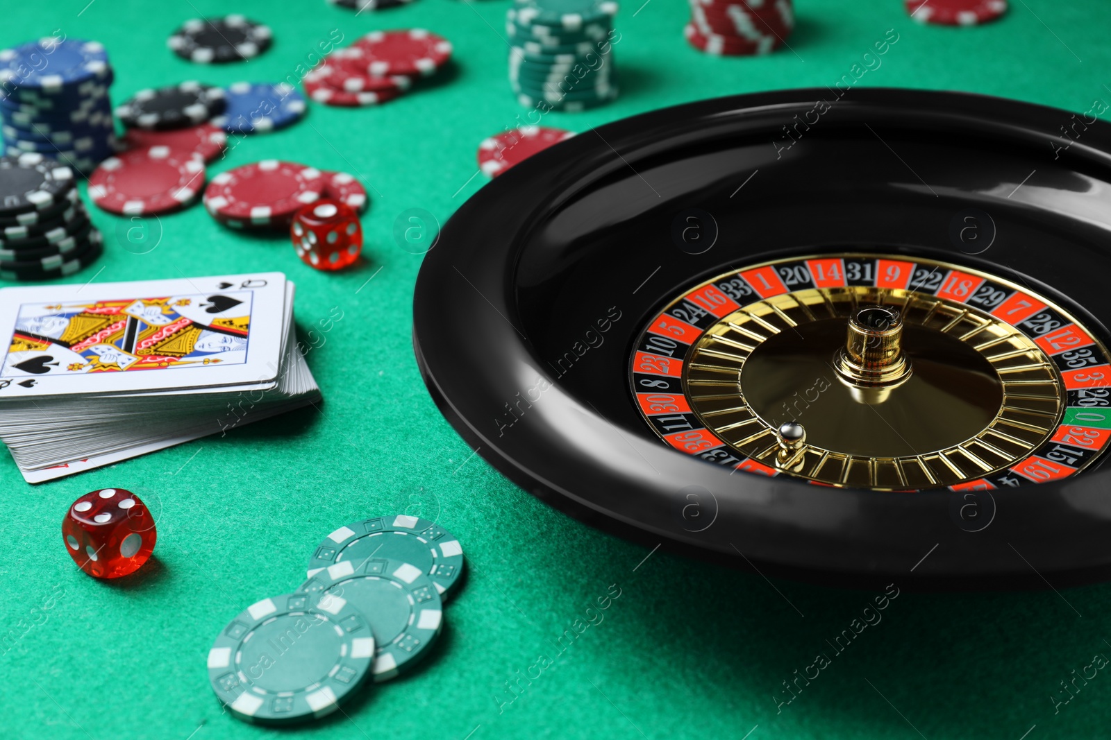 Photo of Roulette wheel, playing cards, chips and dice on green table, closeup. Casino game