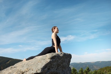 Photo of Beautiful young woman practicing yoga on rock in mountains