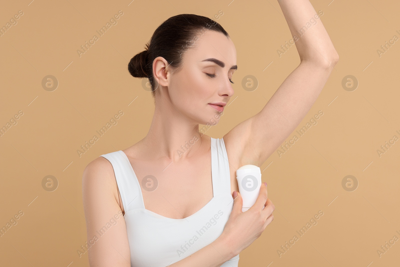 Photo of Beautiful woman applying deodorant on beige background