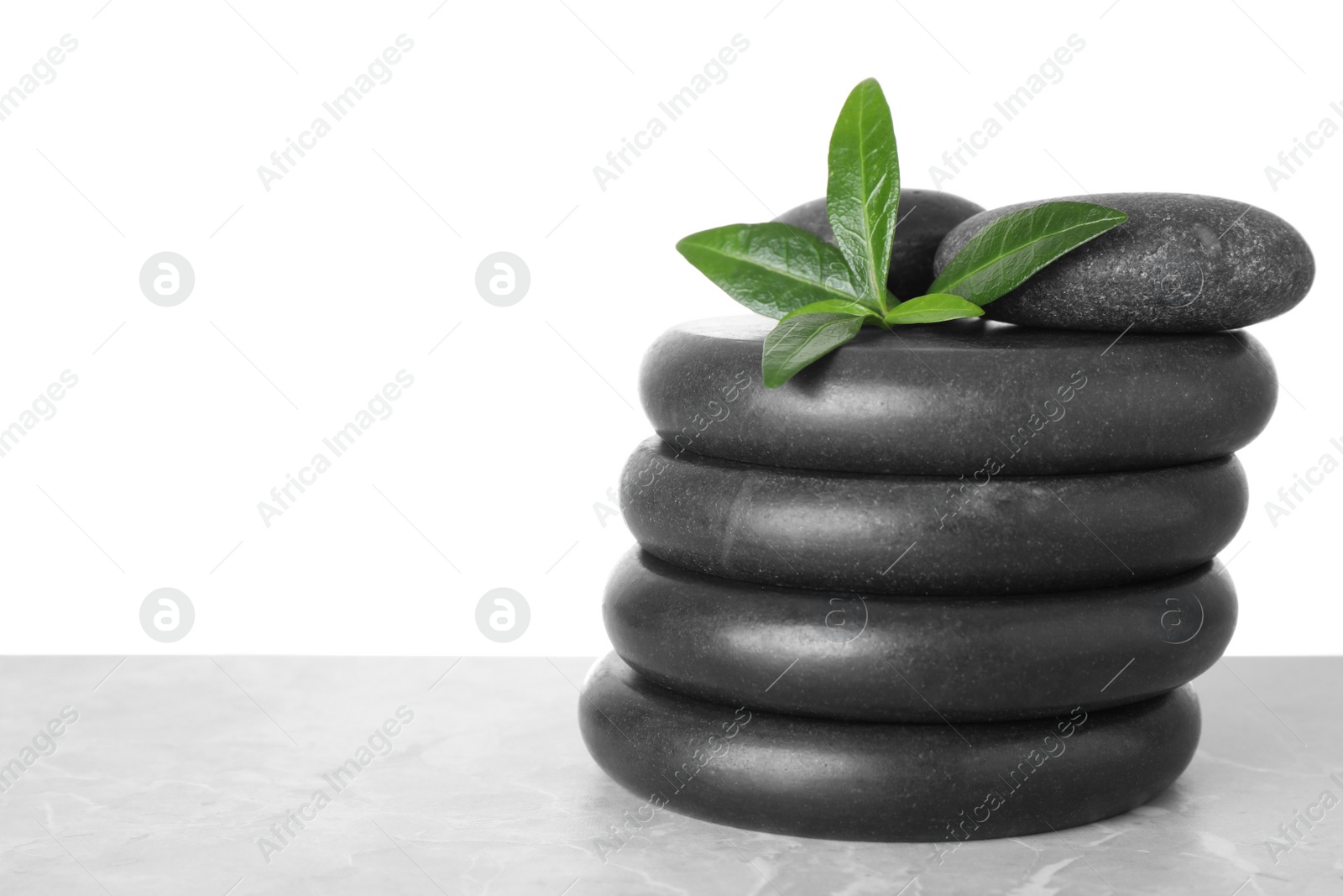 Photo of Stack of spa stones and green leaves on table against white background. Space for text