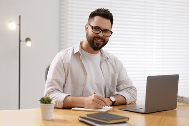 Young man in glasses watching webinar at table in room