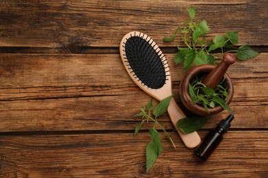 Photo of Stinging nettle extract and brush on wooden background, flat lay with space for text. Natural hair care