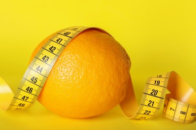 Photo of Cellulite problem. Orange with measuring tape on yellow background, closeup