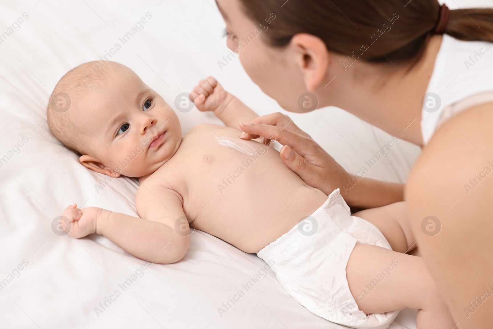 Photo of Woman applying body cream onto baby`s skin on bed, closeup