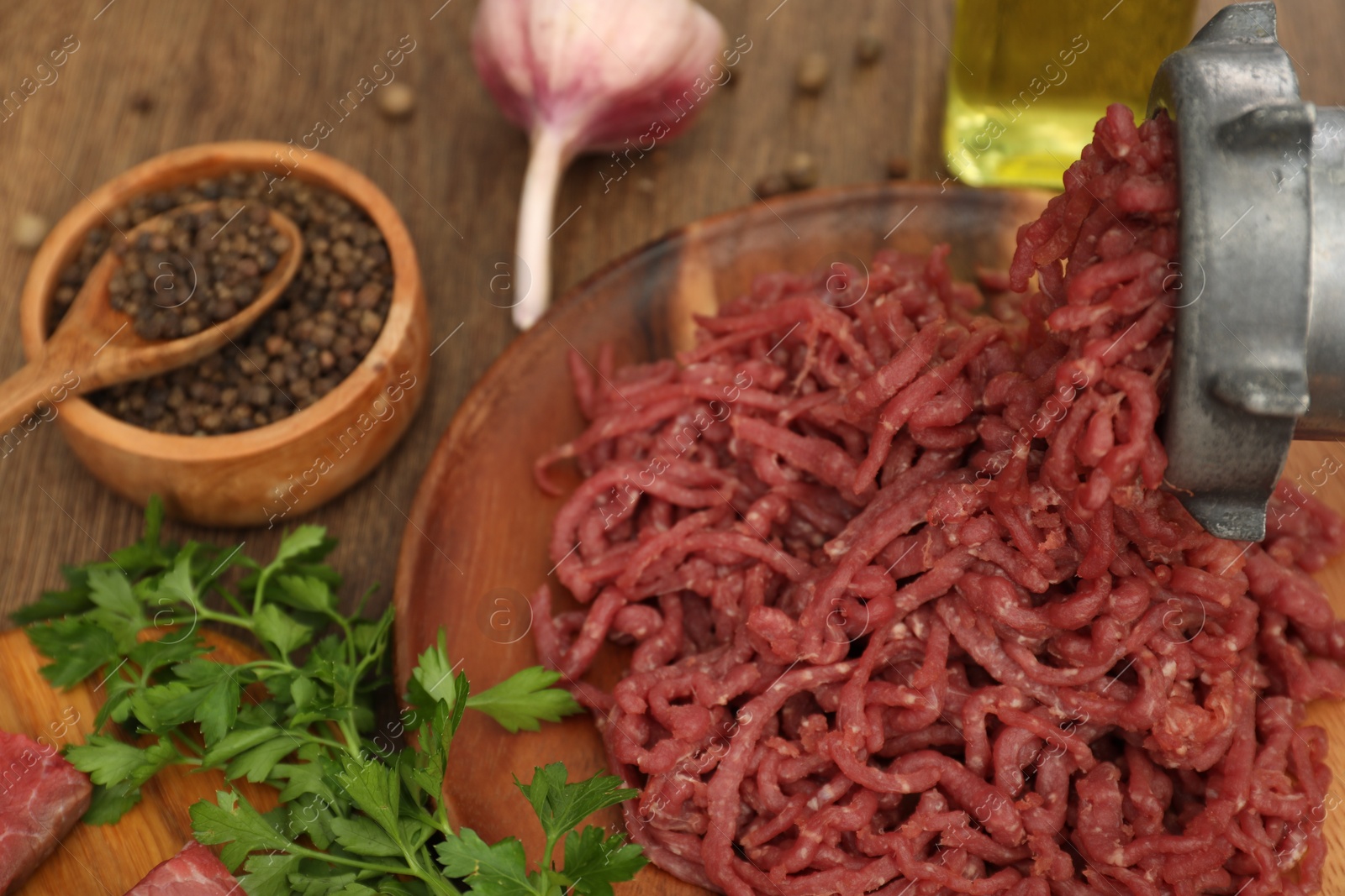 Photo of Meat grinder with beef mince, garlic, parsley and peppercorns on wooden table, closeup