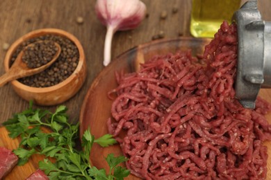 Meat grinder with beef mince, garlic, parsley and peppercorns on wooden table, closeup