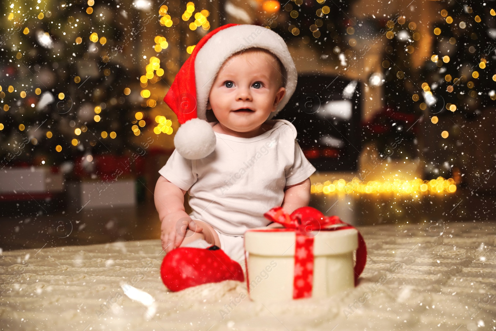 Image of Cute baby in Santa hat with Christmas gift on floor at home