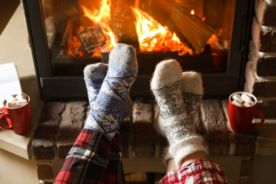 Photo of Couple in pajamas resting near fireplace indoors, closeup. Winter vacation