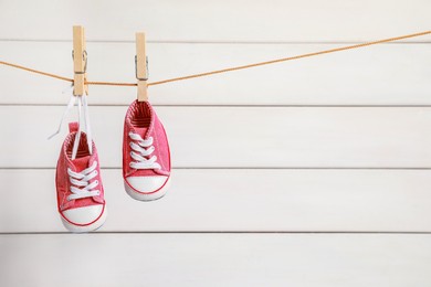 Photo of Cute pink baby sneakers drying on washing line against white wall. Space for text