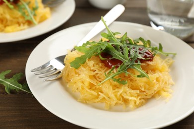 Photo of Tasty spaghetti squash with tomato sauce and arugula served on wooden table, closeup