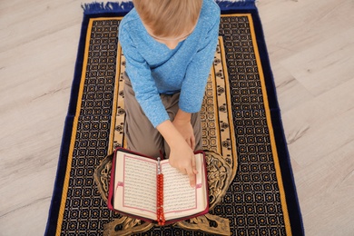 Photo of Little Muslim boy reading Koran on prayer rug indoors