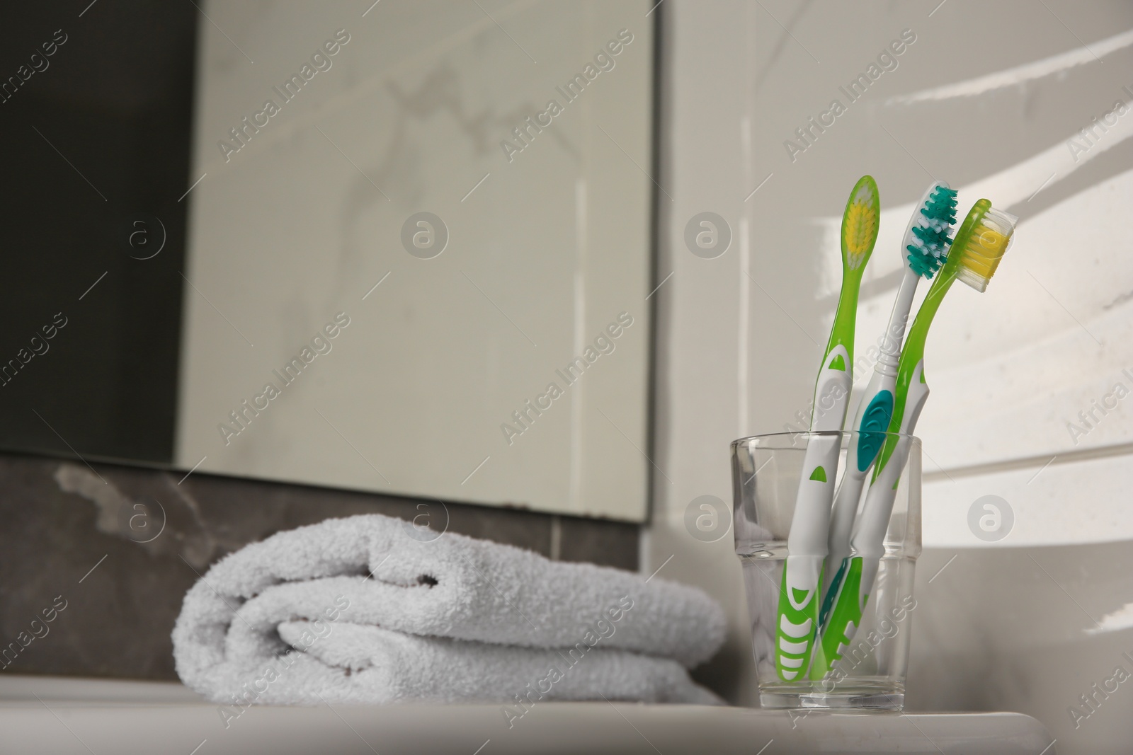Photo of Colorful toothbrushes in glass holder and terry towel on table indoors
