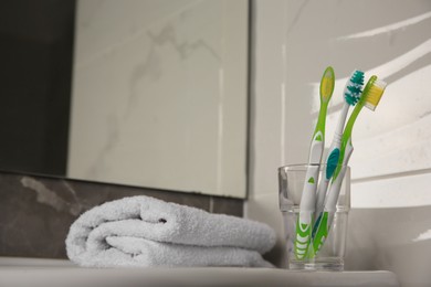 Colorful toothbrushes in glass holder and terry towel on table indoors