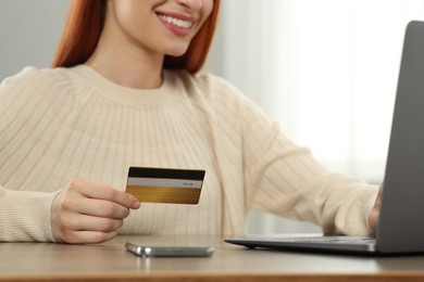 Photo of Woman with credit card using laptop for online shopping at wooden table indoors, closeup