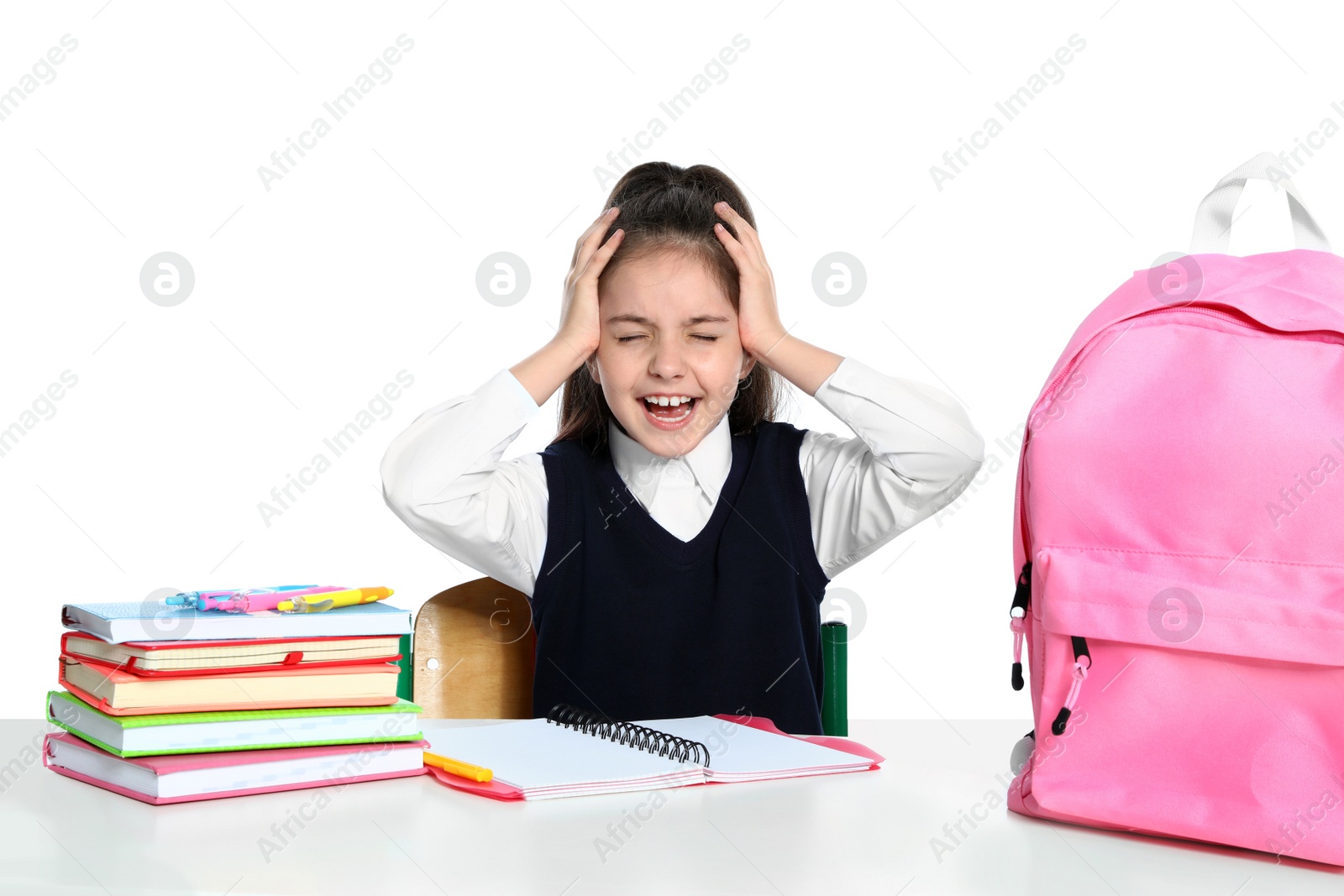 Photo of Emotional little girl in uniform with school stationery at desk against white background