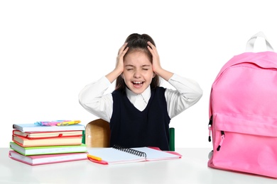 Emotional little girl in uniform with school stationery at desk against white background