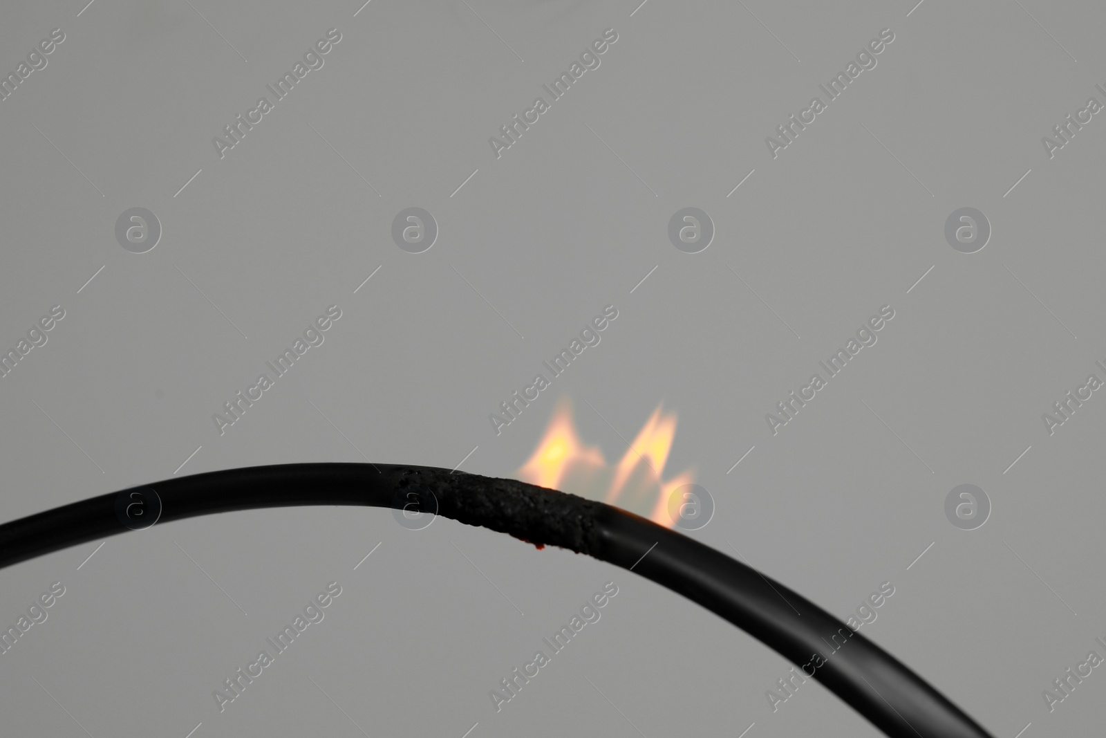 Photo of Inflamed black wire on grey background, closeup. Electrical short circuit