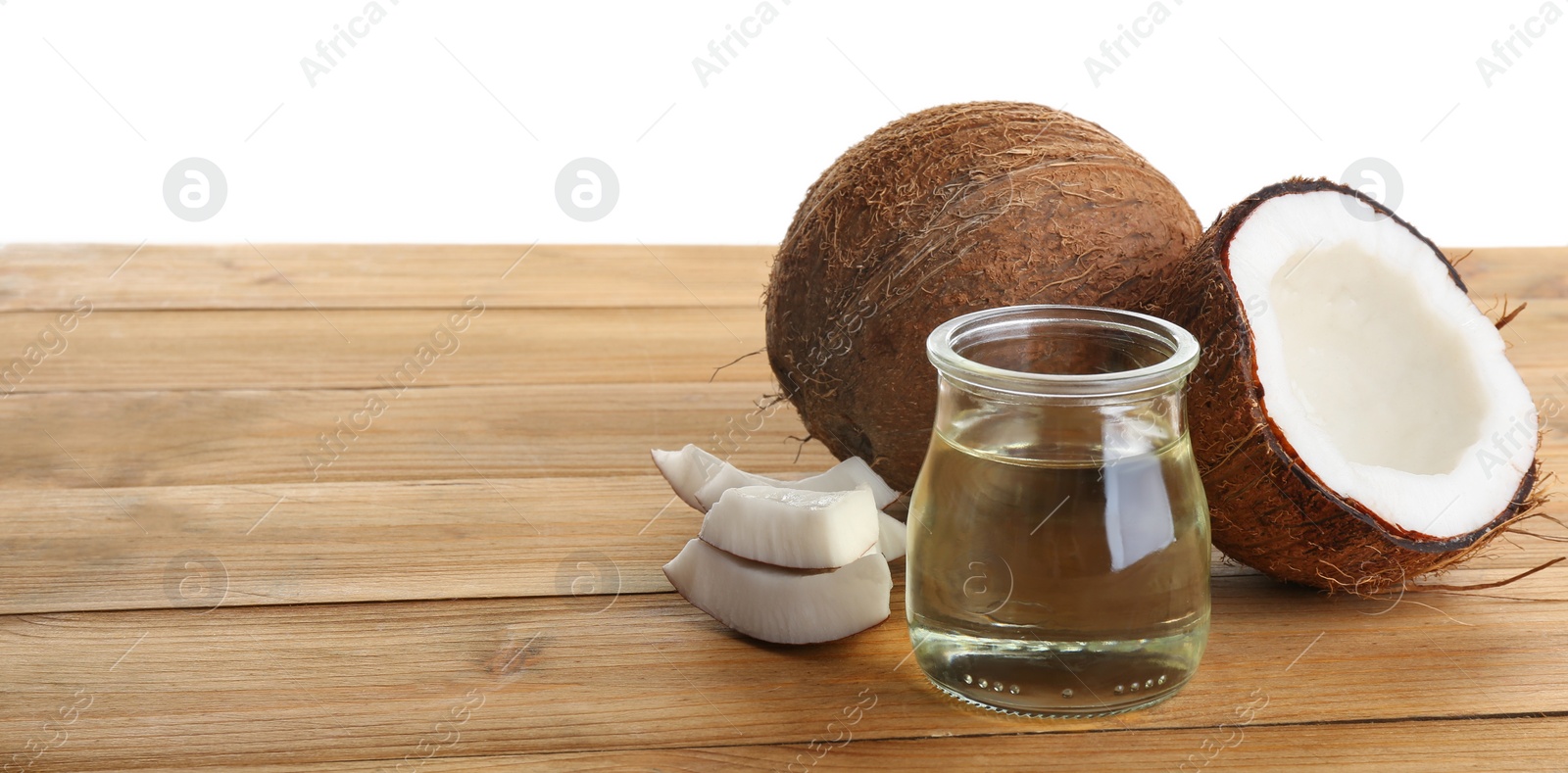 Photo of Ripe coconuts and jar with natural organic oil on wooden table against white background