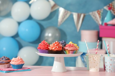 Different colorful cupcakes and party accessories on pink table