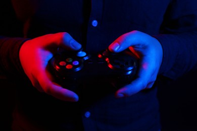 Photo of Man using wireless game controller on dark background in neon lights, closeup