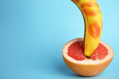 Photo of Fresh banana with red lipstick marks and grapefruit on blue background, space for text. Sex concept