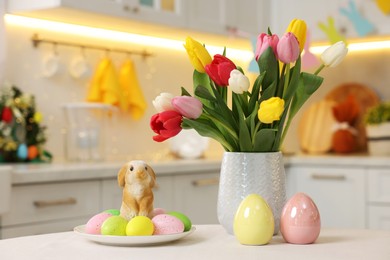 Photo of Bouquet of tulips, painted eggs and Easter decorations on white table in kitchen