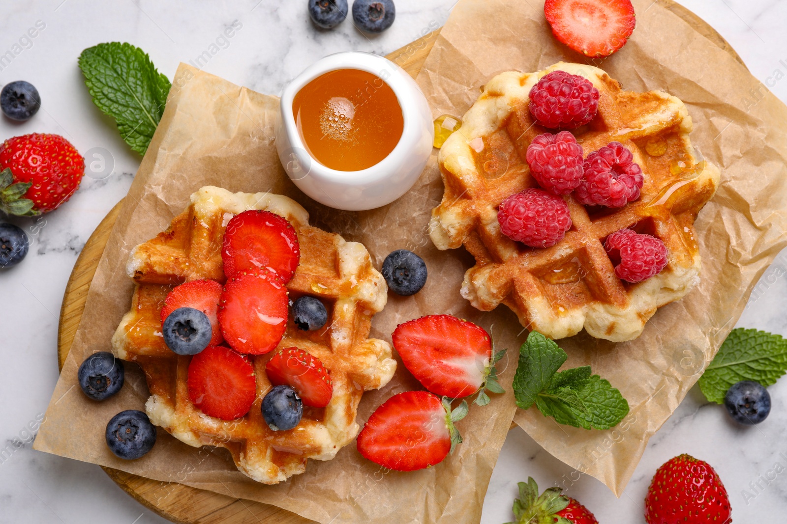 Photo of Delicious Belgian waffles with fresh berries and honey on white marble table, flat lay