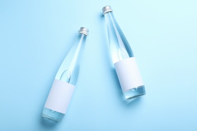Photo of Glass bottles of water with blank label on light blue background, flat lay