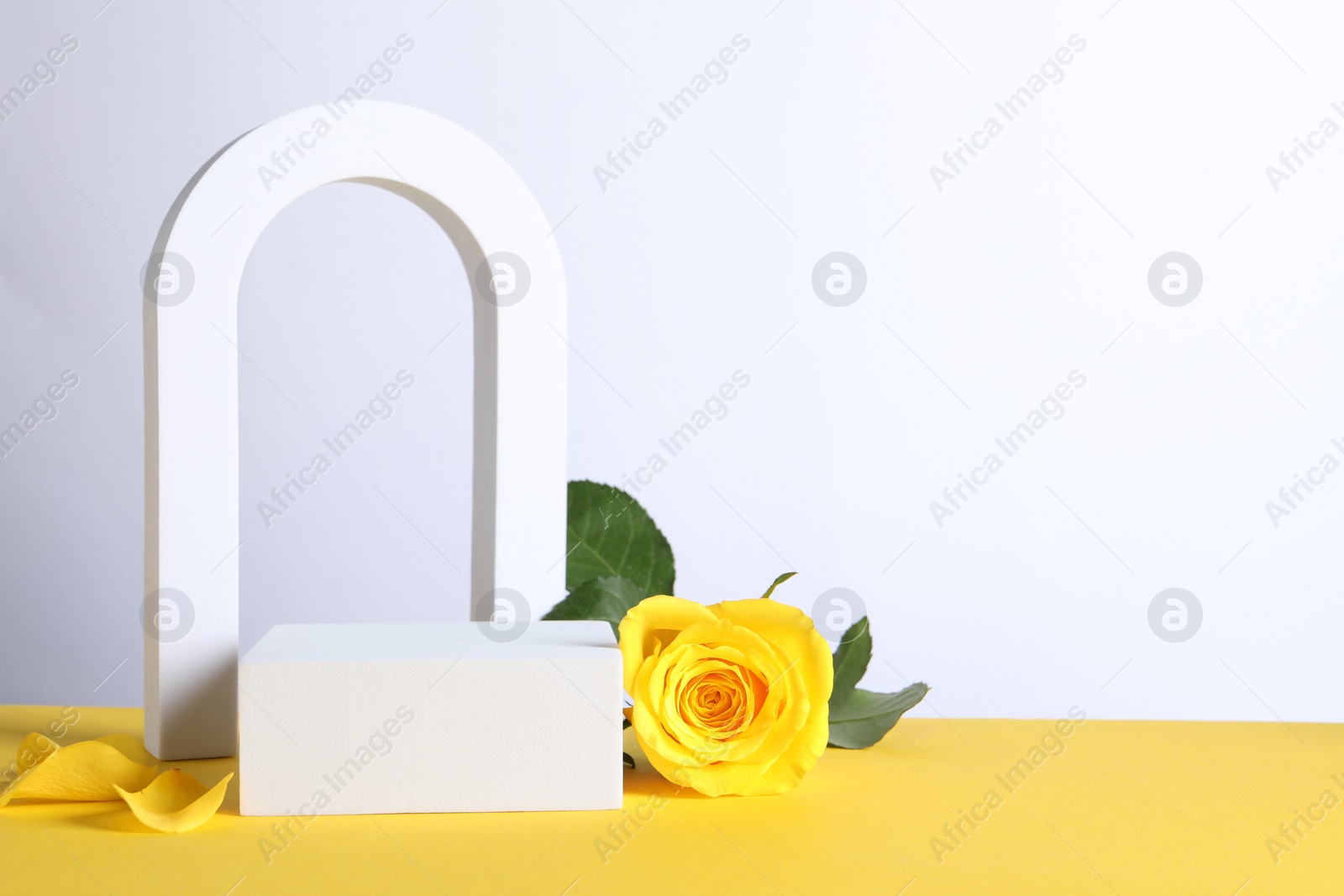 Photo of Beautiful presentation for product. Geometric figures and rose on yellow table against white background, space for text