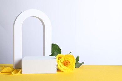 Photo of Beautiful presentation for product. Geometric figures and rose on yellow table against white background, space for text