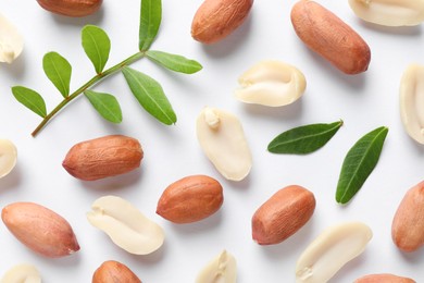 Photo of Fresh peanuts and green leaves on white background, flat lay
