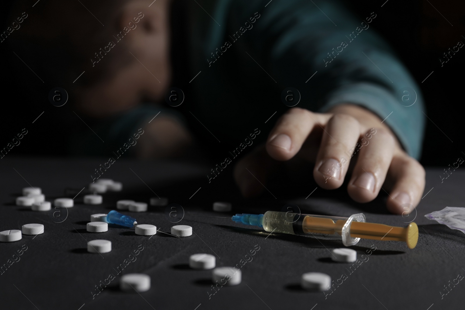 Photo of Addicted man reaching to drugs at black table, focus on syringe