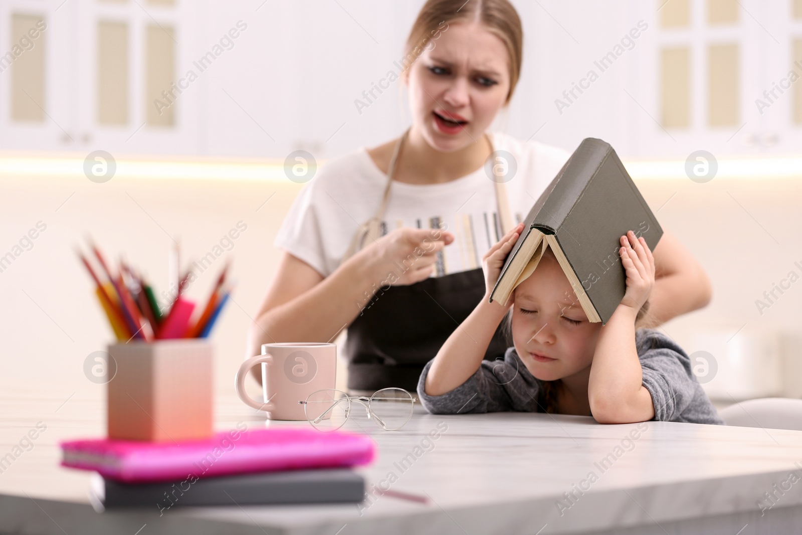 Photo of Mother scolding her daughter while helping with homework in kitchen