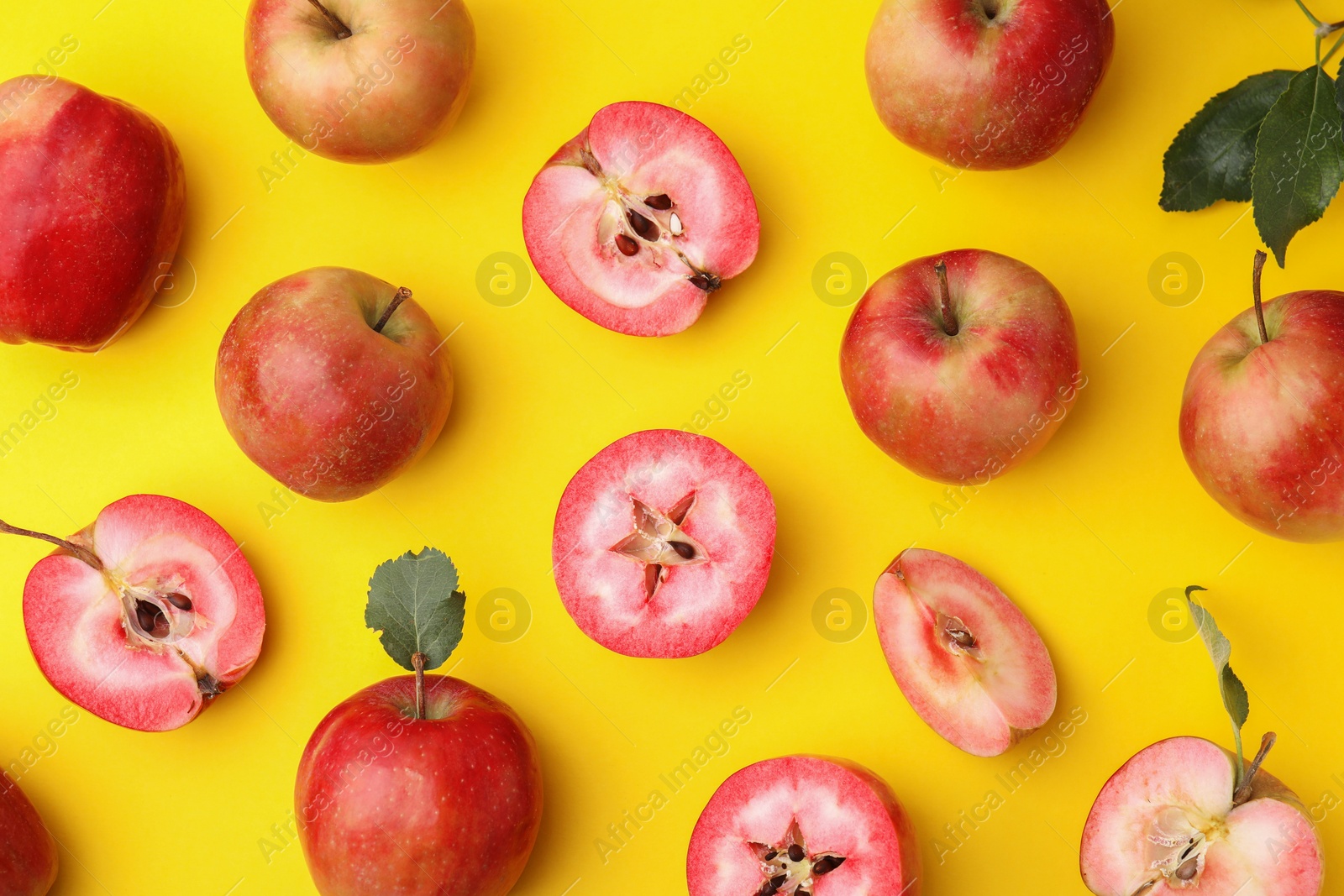 Photo of Tasty apples with red pulp and leaves on yellow background, flat lay