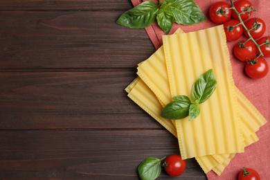 Photo of Uncooked lasagna sheets with cherry tomatoes and basil on wooden table, flat lay. Space for text