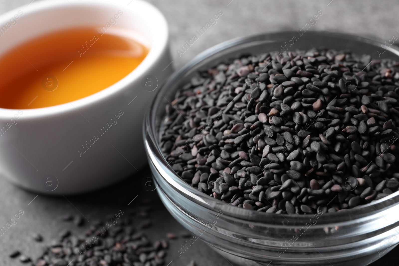 Photo of Black sesame seeds and oil on grey table, closeup