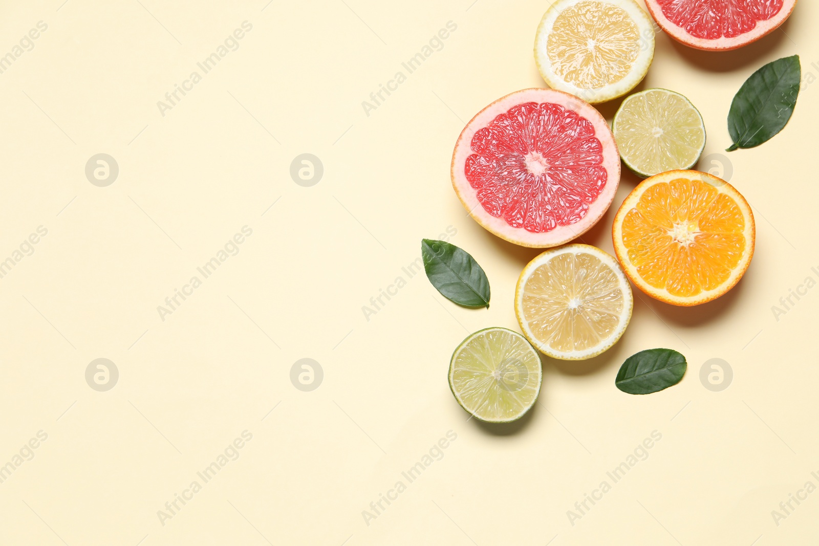 Photo of Different cut citrus fruits and leaves on beige table, flat lay. Space for text