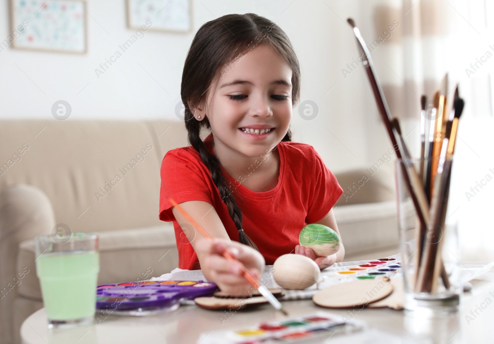Photo of Little girl painting decorative egg at table indoors. Creative hobby
