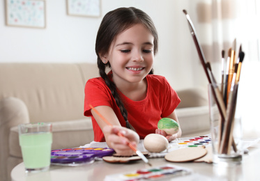 Little girl painting decorative egg at table indoors. Creative hobby